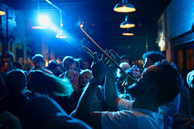 A man plays the trumpet in a dimly lit bar surrounded by people