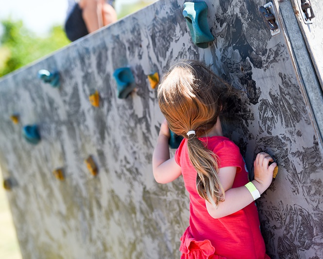 A young girl climbs a climbing wall at Armed Forces Day event in 2018.