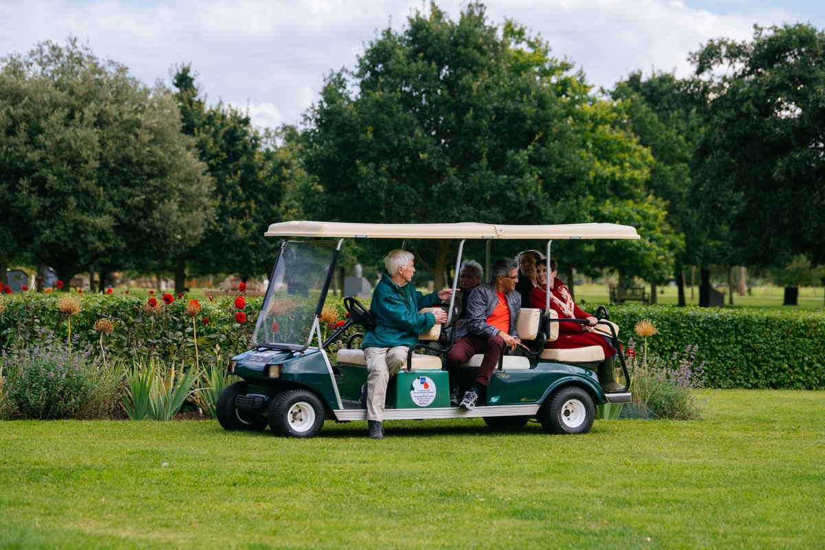 A group of adults, sitting on a golf buggy, listen to an Arboretum volunteer as he delivers a talk from a golf buggy