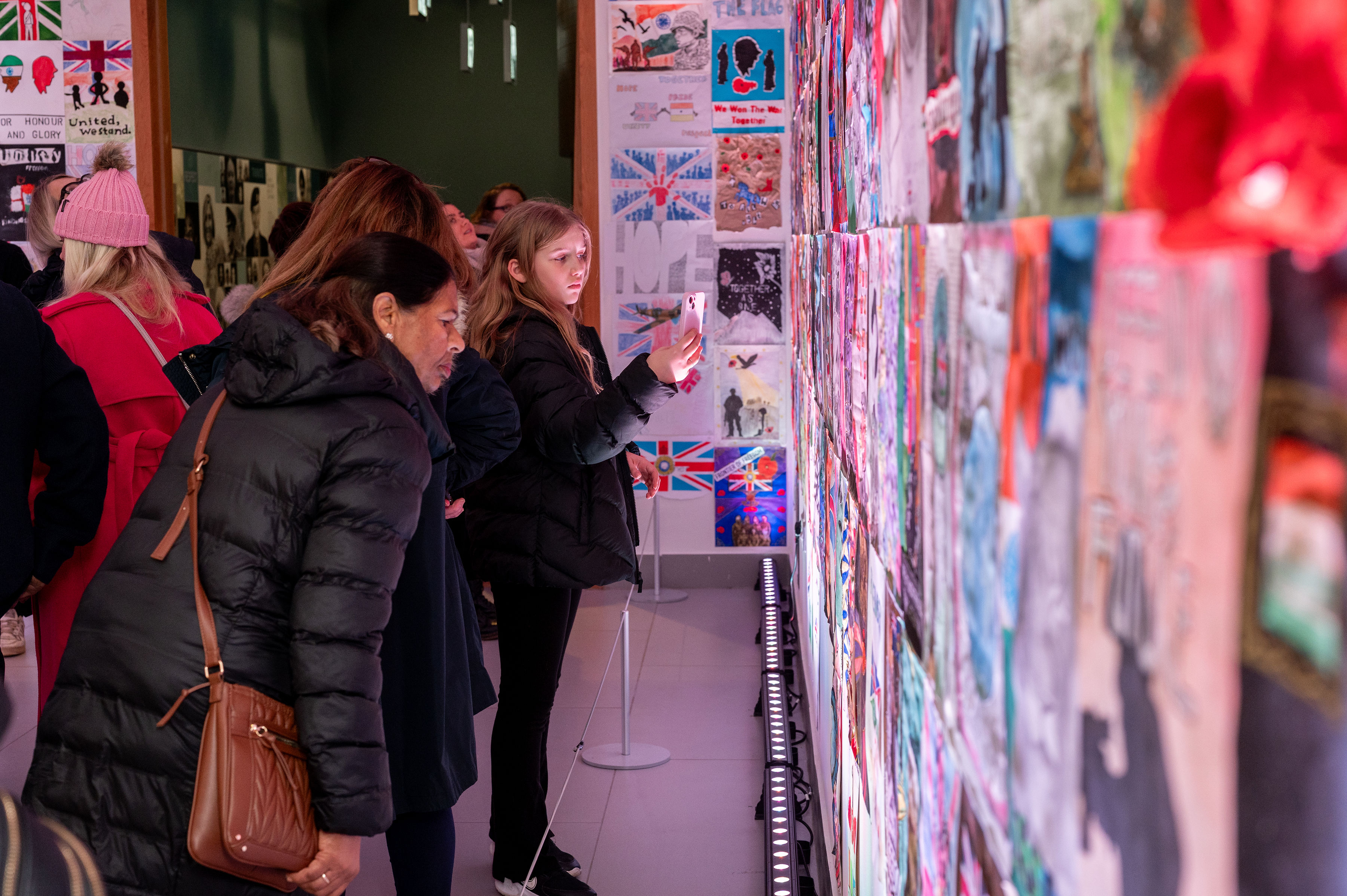 People pointing out posters that line the gallery wall as part of the Forgotten Army exhibition in 2025.