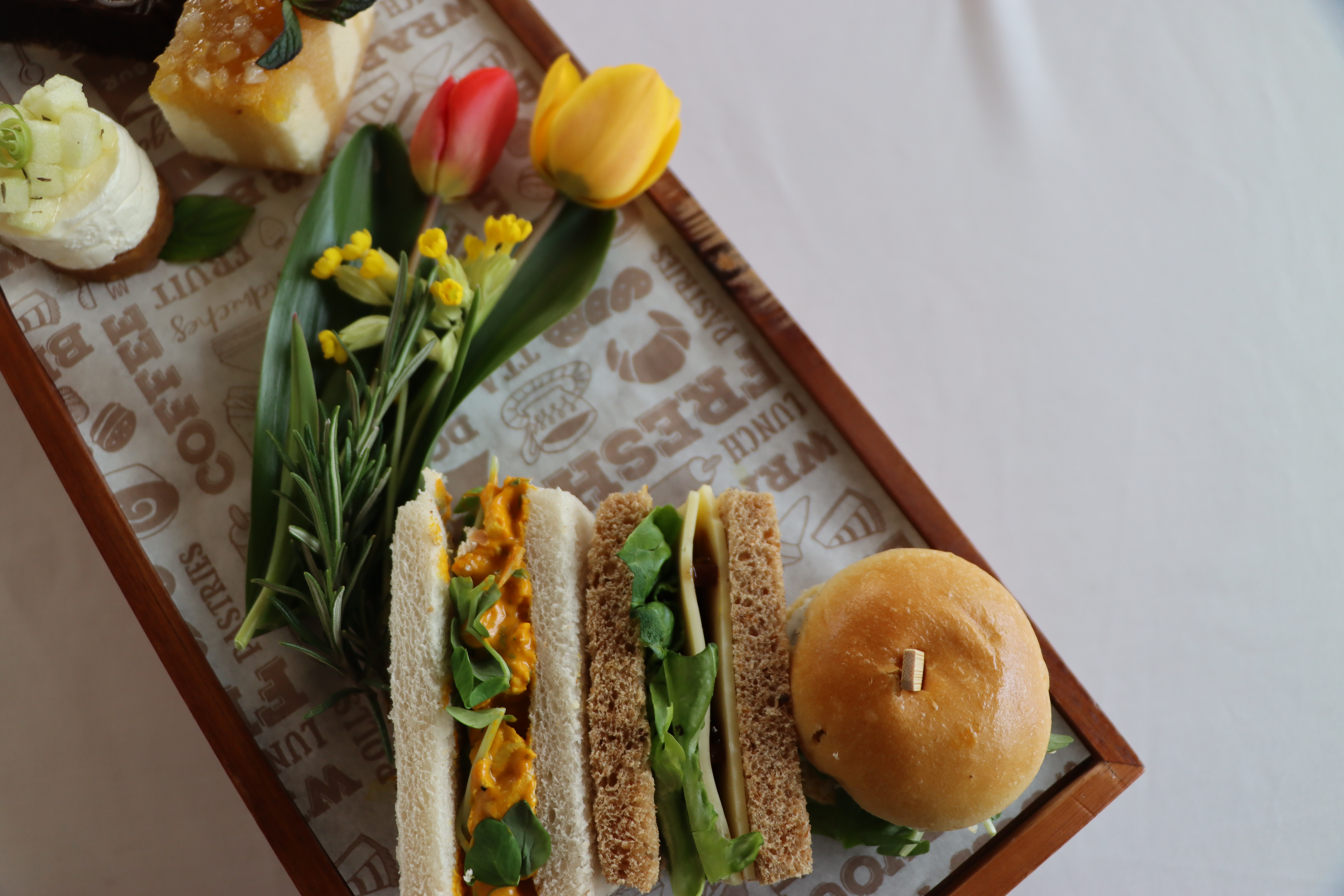 25th anniversary afternoon tea on a wooden board, prepared in celebration of the arboretums anniversary. There are sandwiches, cakes and fresh scones.